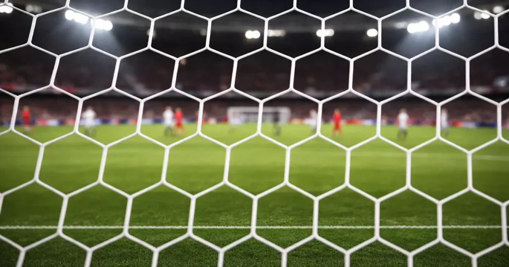 Rete di una porta da calcio vista da dietro con il campo verde illuminato dai riflettori sullo sfondo
